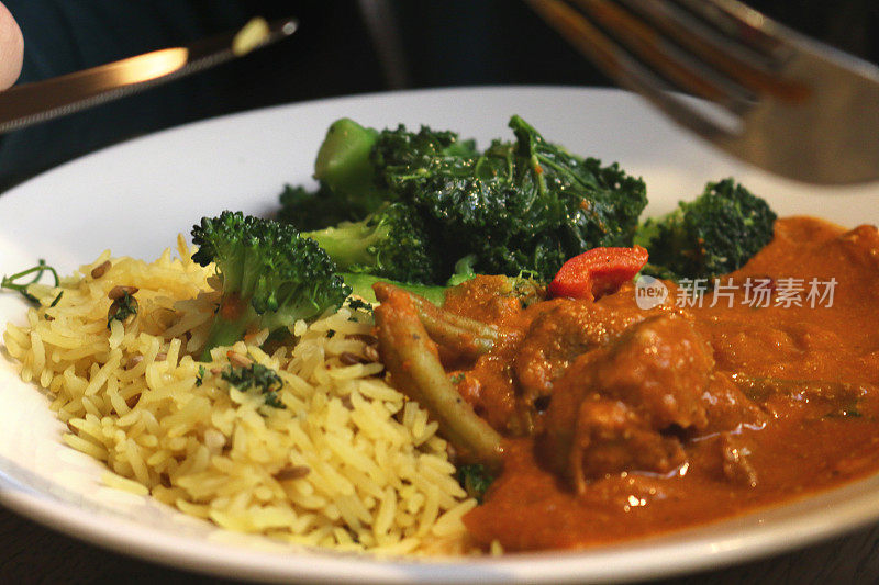 想象一下，在外面吃自制的印度餐馆食物:烤鸡肉、黄色藏红花味的肉饭、绿色蔬菜和花椰菜在木制餐桌上，男人用刀叉餐具吃健康的咖喱酒吧午餐/晚餐